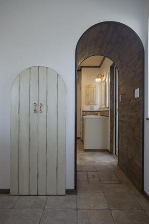 トンネルアーチをくぐれば洗面室へ。階段下収納の扉はエイジング仕上げで。